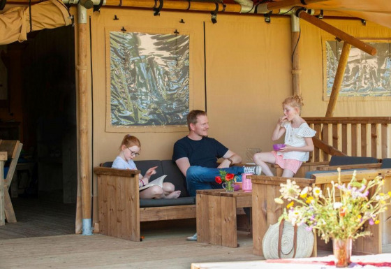 Familia relajándose en la terraza de la tienda Safari Meddo con muebles de madera y flores.
