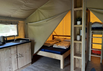 Interior de la tienda Safari Mill en Camping Sevink Molen, Países Bajos, con camas, litera y cocina.