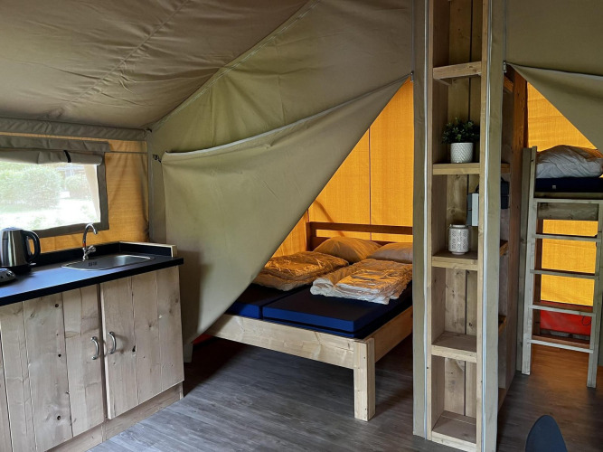 Interior de la tienda Safari Mill en Camping Sevink Molen, Países Bajos, con camas, litera y cocina.