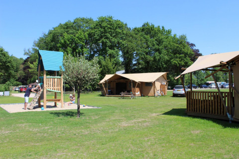 Familias jugando junto a tiendas safari y parque infantil en Camping Sevink Molen, Países Bajos, día soleado.