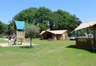Familias jugando junto a tiendas safari y parque infantil en Camping Sevink Molen, Países Bajos, día soleado.