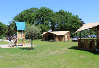 Famiglie giocano vicino a tende safari e area giochi al Camping Sevink Molen, Olanda, in una giornata soleggiata.