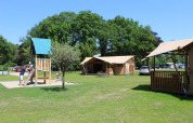 Familias jugando junto a tiendas safari y parque infantil en Camping Sevink Molen, Países Bajos, día soleado.