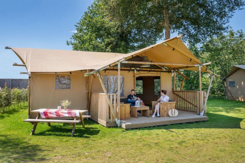 Twee personen zitten op de veranda van safaritent Hilgelo, omringd door natuur en zonlicht.