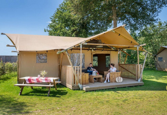Twee personen zitten op de veranda van safaritent Hilgelo, omringd door natuur en zonlicht.