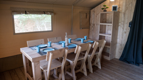 Dining area inside Safaritent at Camping Het Veen in Belgium, featuring wooden furniture and blue tableware.