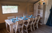 Dining area inside Safaritent at Camping Het Veen in Belgium, featuring wooden furniture and blue tableware.