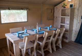 Dining area inside Safaritent at Camping Het Veen in Belgium, featuring wooden furniture and blue tableware.