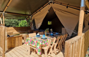 Tienda safari con terraza de madera cubierta y mesa con mantel colorido en Domaine La Sauzette, Francia