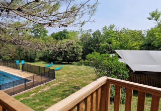 Zicht vanaf een houten terras op een omheind zwembad, blauwe ligzetels en safaritent in Frankrijk.