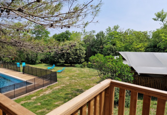 Blick von einer Holzterrasse auf einen Pool mit Zaun, blaue Liegestühle und Safarizelt in Frankreich.