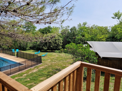 Blick von einer Holzterrasse auf einen Pool mit Zaun, blaue Liegestühle und Safarizelt in Frankreich.
