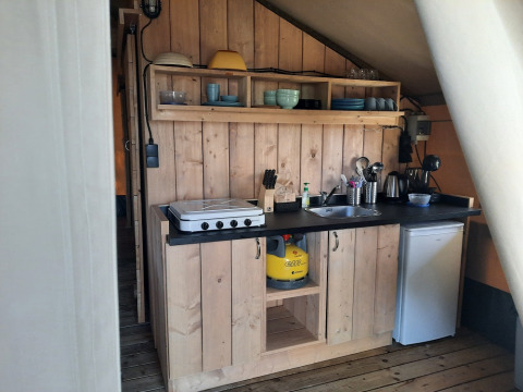 Area cucina in una tenda safari al Domaine La Sauzette, Francia, con mobili in legno e fornello a gas.