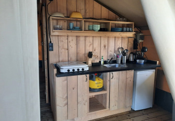Area cucina in una tenda safari al Domaine La Sauzette, Francia, con mobili in legno e fornello a gas.