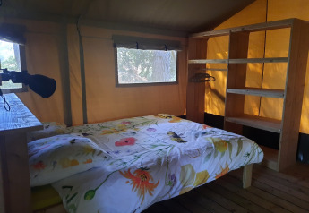 Interior de una tienda safari con cama doble, estantería y ventana en Domaine La Sauzette, Francia.