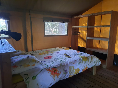 Interior of a safari tent with a double bed, shelving unit and window at Domaine La Sauzette in France.