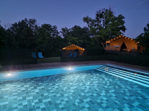 Beleuchtetes Schwimmbad bei Sonnenuntergang mit Safarizelten und Lichterketten in Domaine La Sauzette, Frankreich.