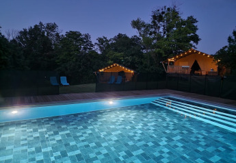 Piscina iluminada al anochecer con tiendas safari y luces en Domaine La Sauzette, Francia.
