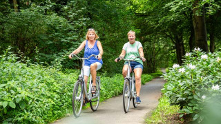 Dos mujeres pasean en bicicleta por un sendero arbolado en Bospark Ede, un parque en Gelderland, Países Bajos.