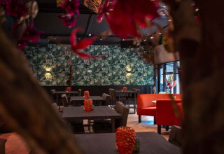 Interior of a restaurant with green foliage walls and red seating at Bospark Ede holiday park, Gelderland, Netherlands.