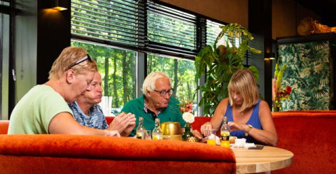 Vier ältere Personen sitzen gemeinsam an einem runden Tisch im Bospark Ede Ferienpark in Gelderland, Niederlande.