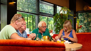Cuatro personas mayores disfrutan de una comida junta en un restaurante en Bospark Ede, Gelderland, Países Bajos.