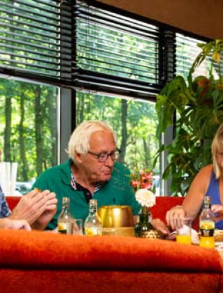 Cuatro personas mayores disfrutan de una comida junta en un restaurante en Bospark Ede, Gelderland, Países Bajos.
