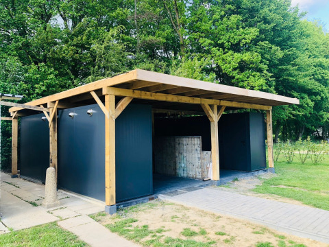 Modern camping building with wooden frame and gray walls at Camping de Boskant, Limburg, Netherlands, surrounded by trees.