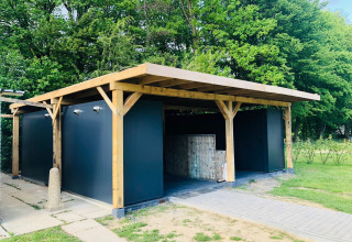 Modern camping building with wooden frame and gray walls at Camping de Boskant, Limburg, Netherlands, surrounded by trees.