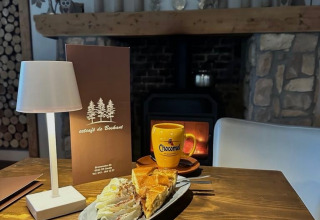 Atmosfera accogliente con cioccolata calda, torta e panna vicino al camino a Camping de Boskant, Limburg.