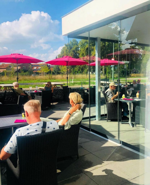 Buitenterras met mensen onder roze parasols bij Camping de Boskant, Limburg, Nederland.