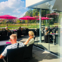 Außencafé mit Menschen unter pinken Sonnenschirmen im Camping de Boskant, Limburg, Niederlande.