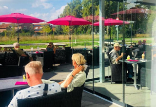 Udendørs caféområde med folk under lyserøde parasoller på Camping de Boskant, Limburg, Holland.