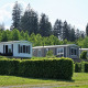 Tre chalet-hytter på Camping & Ferienpark Brilon, omgivet af grønne hække og skov i Tyskland.