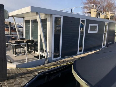 Moderne woonboot in Marina Parcs - Jachthaven De Hoop, Noord-Holland, Nederland met terras en stoelen.