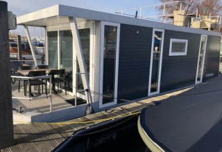 Moderne woonboot in Marina Parcs - Jachthaven De Hoop, Noord-Holland, Nederland met terras en stoelen.
