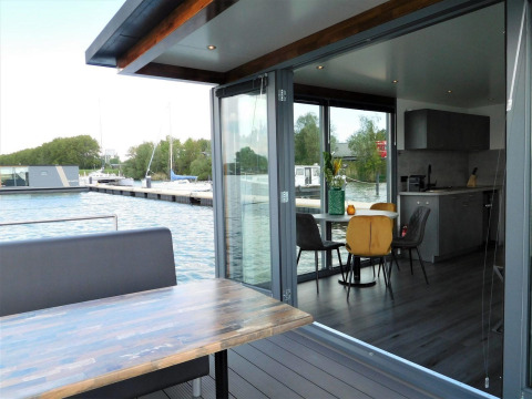 Moderne woonboot met eetplaats op het dek en zicht op de jachthaven bij Jachthaven De Hoop, Noord-Holland.