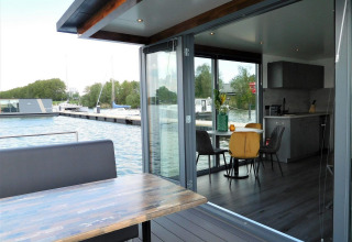 Moderne woonboot met eetplaats op het dek en zicht op de jachthaven bij Jachthaven De Hoop, Noord-Holland.