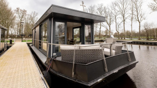 Casa flotante moderna con terraza amarrada al muelle, rodeada de árboles en Friesland, Países Bajos.