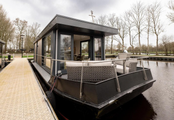 Casa flotante moderna con terraza amarrada al muelle, rodeada de árboles en Friesland, Países Bajos.