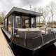 Moderne husbåd med terrasse fortøjet ved dock, omkranset af træer i Friesland, Holland.