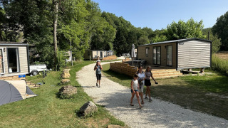 Mensen lopen op een grindpad tussen stacaravans bij Mobilhome Toulouse, La Draille in Frankrijk, met veel groen.