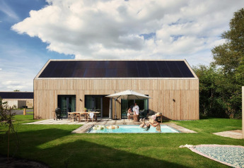 Unbrick One-lodge med sauna, pool og solpaneler, familie hygger sig udendørs i moderne træhytte.