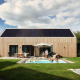 Unbrick One-lodge med sauna, pool og solpaneler, familie hygger sig udendørs i moderne træhytte.