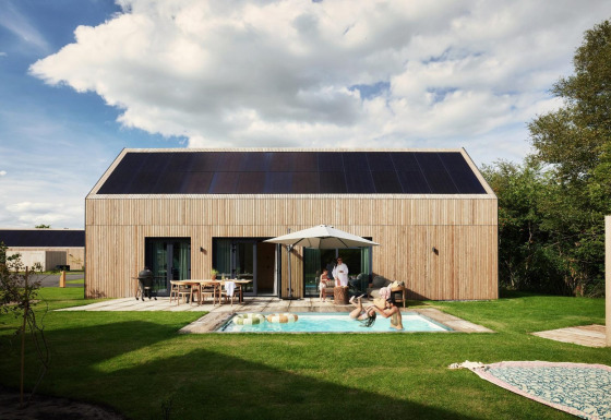 Unbrick One lodge with sauna, pool, and solar panels, family relaxing outdoors at modern wooden cabin.