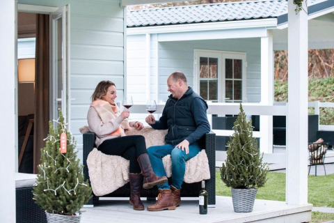 Couple enjoying wine on the porch at Verandah Chalet, Camping Sevink Molen in the Netherlands, cozy scene.