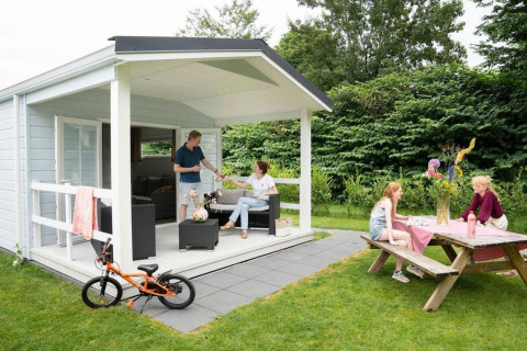 Famiglia che si gode il glamping in una piccola casa con veranda e tavolo da picnic in giardino verde.