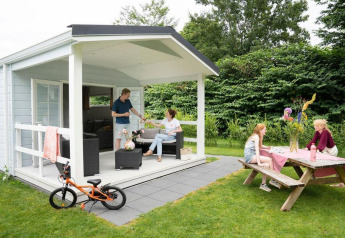 Famiglia che si gode il glamping in una piccola casa con veranda e tavolo da picnic in giardino verde.