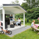 Familie nyder glamping ved et lille hyttehus med veranda og picnicbord i en grøn have.
