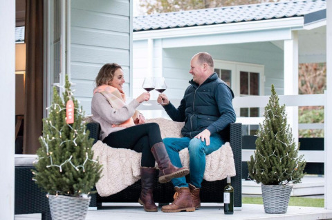 Couple enjoys red wine together on the porch of Verandah Chalet at Camping Sevink Molen, Netherlands.